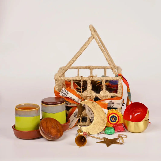 Festive Joy Gift Hamper with Jute Basket, Brass Diyas, Ceramic Tumblers with Dry Fruits, Metal Windchime & Seed Crackers The confetti tree