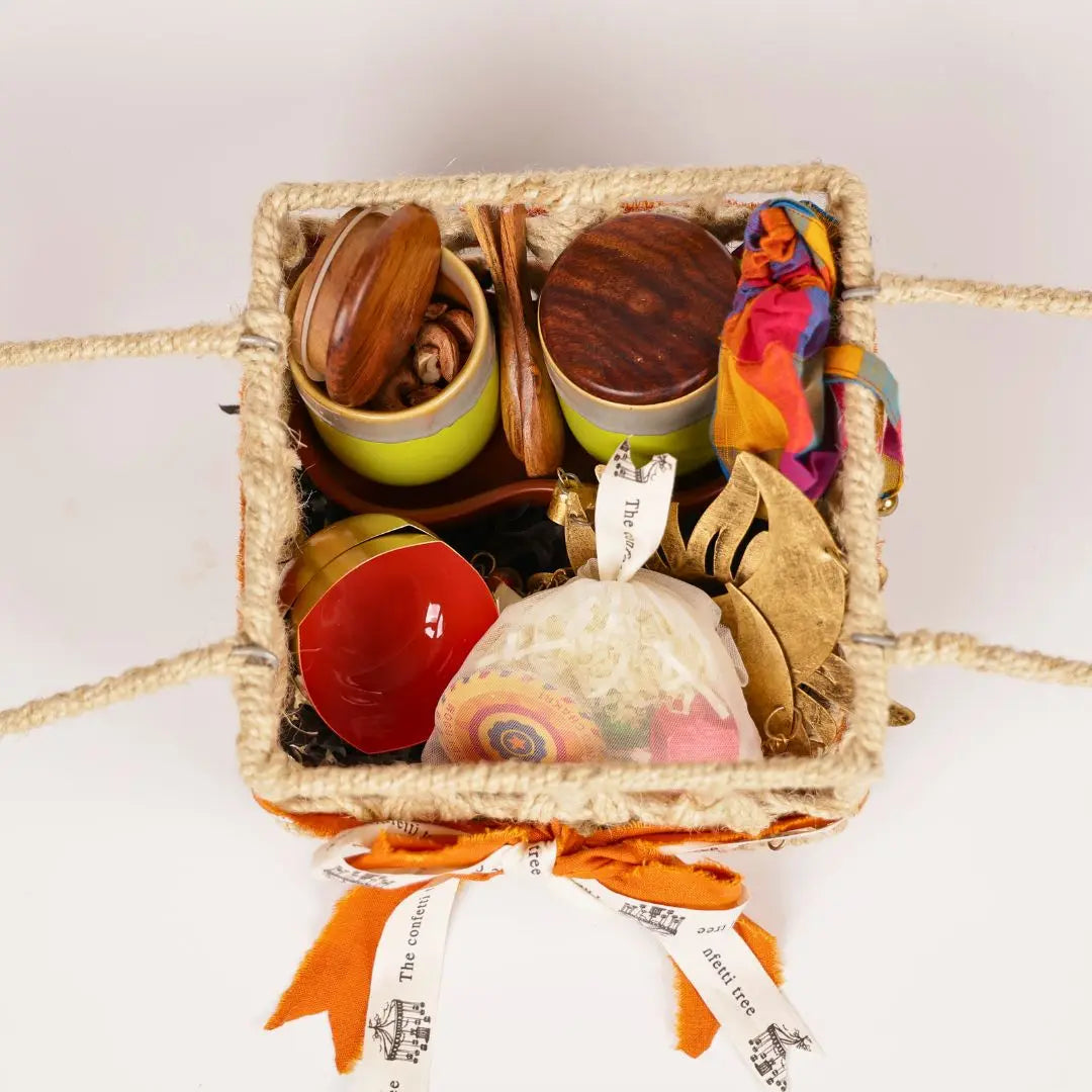 Festive Joy Gift Hamper with Jute Basket, Brass Diyas, Ceramic Tumblers with Dry Fruits, Metal Windchime & Seed Crackers The confetti tree