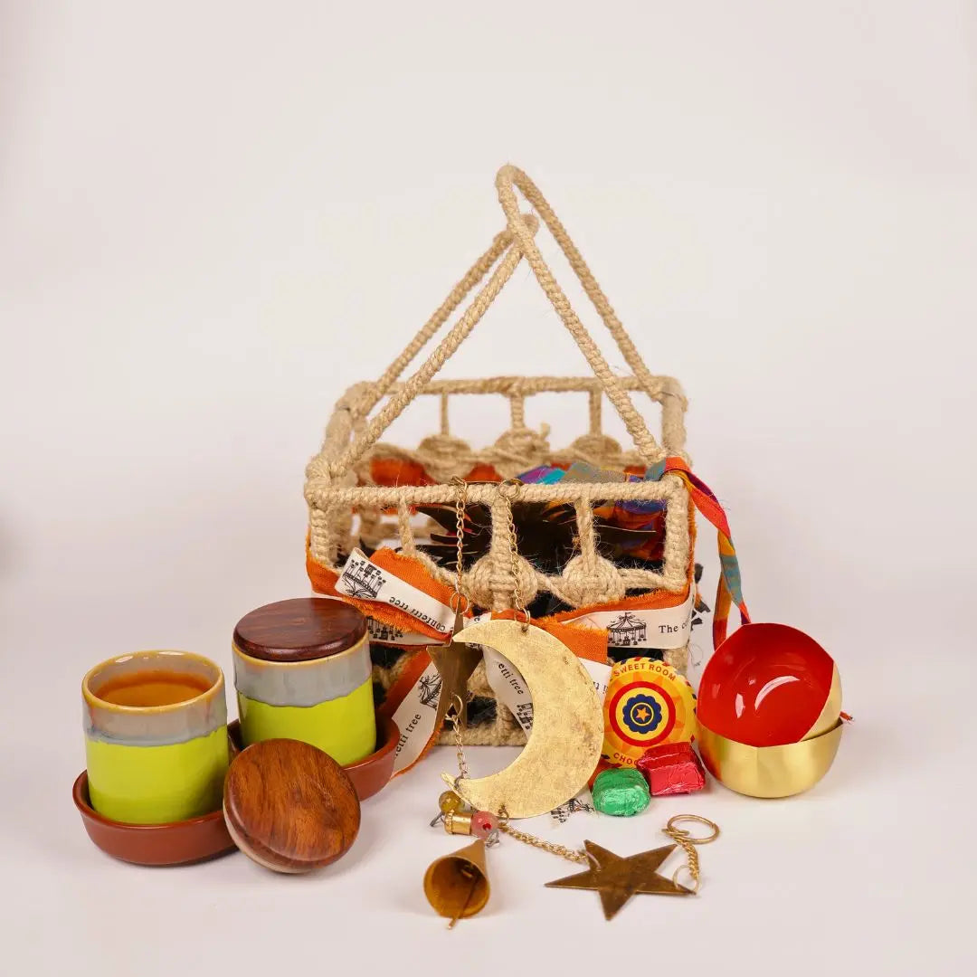 Festive Joy Gift Hamper with Jute Basket, Brass Diyas, Ceramic Tumblers with Dry Fruits, Metal Windchime & Seed Crackers The confetti tree