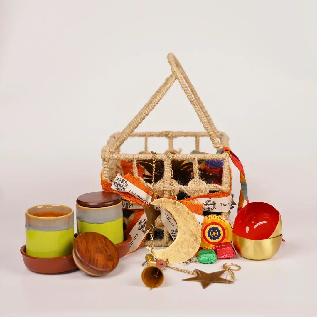 Festive Joy Gift Hamper with Jute Basket, Brass Diyas, Ceramic Tumblers with Dry Fruits, Metal Windchime & Seed Crackers The confetti tree
