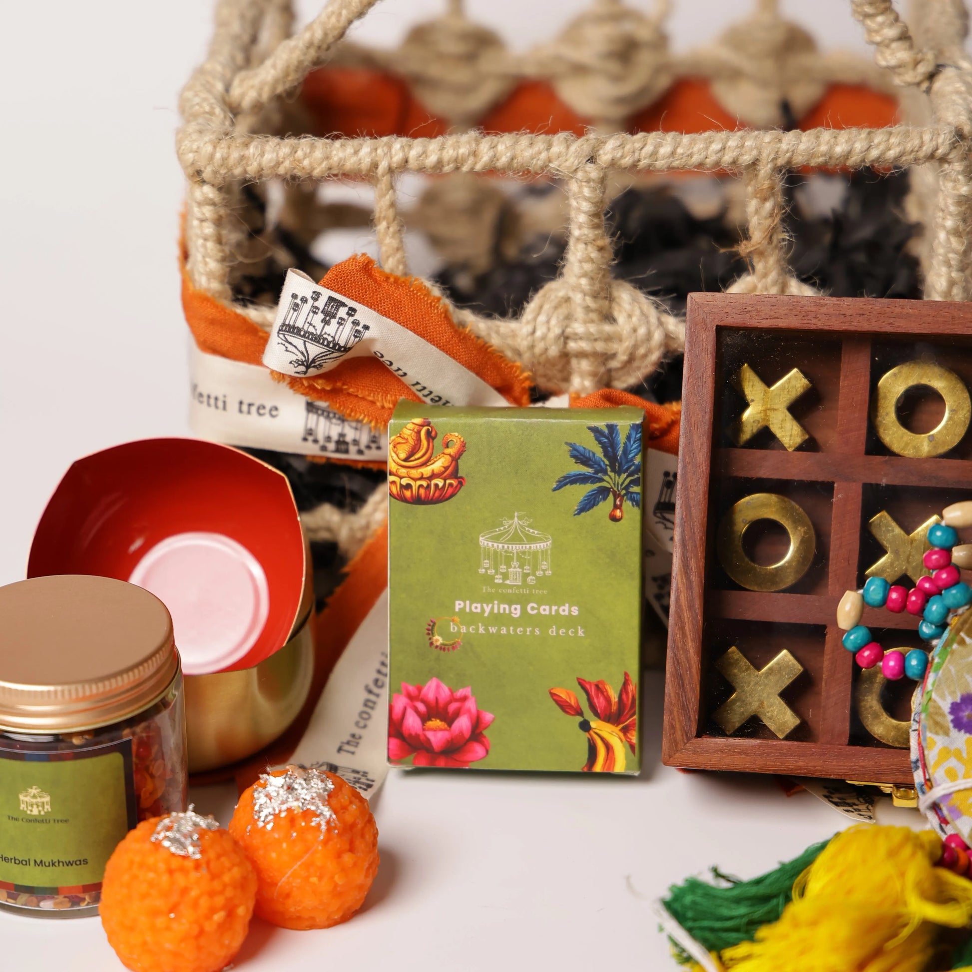 Luxury Jute Gift Basket with Wooden Tic Tac Toe, Brass Diyas, Toran, Laddoo Candles, Mukhwas Jar & Playing Cards – Festive Gifting Hamper The confetti tree